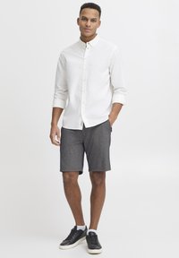 White long-sleeve button-up shirt, gray textured shorts, and black sneakers. Simple design, no patterns, with a clean and casual look.
