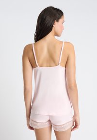 Camiseta de tirantes finos en rosa claro con pantalones cortos a juego que presentan un ribete de encaje. Textura suave y corte relajado, adecuada para ropa de estar en casa.