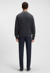 Tummanharmaa pusero resorikauluksella ja -hihoilla, yhdistetty tummansinisiin housuihin, nähtynä takaa. Sileä pinta ja vähäiset yksityiskohdat.