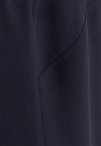 Marinblått tyg med en mjuk, lätt strukturerad yta, som har en subtil böjd sömnadsdetalj. Materialet ser lätt och flytande ut.