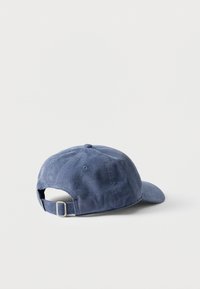 Μπλε καπέλο baseball από κορδόνι που βρίσκεται στο πλάι, δείχνοντας το ρυθμιζόμενο λουρί με μεταλλική αγκράφα σε λευκό φόντο.