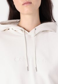 Felpa bianca Calvin Klein realizzata in morbido tessuto, con logo ricamato, cordini con punte metalliche e cappuccio con polsini.