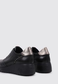 Chaussures en cuir noir avec une semelle en caoutchouc texturée. Accents métalliques argentés sur le talon, ornés de clous décoratifs sur le côté.