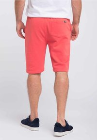 Pantaloni sportivi corallo realizzati in tessuto morbido, con una tasca posteriore e una vestibilità comoda, abbinati a sneakers blu navy.