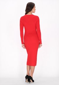 Abito midi rosso a coste con maniche lunghe, silhouette aderente, collo rotondo e orli delle maniche a onda. Indossato con tacchi a spillo neri.