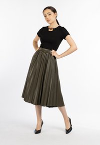 Zwarte fitted top met korte mouwen, gecombineerd met een knielange olijfgroene geplooide rok. Zwarte hoge hakken maken de outfit compleet.