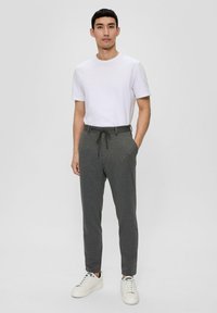 Graue Jogginghosen mit einem Kordelzugbund, kombiniert mit einem schlichten weißen T-Shirt und weißen Sneakers. Glatter Stoff, taillierter Schnitt.