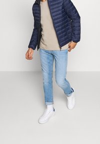 Námořnická prošívaná bunda, béžové tričko, světle modré džíny a bílé tenisky s modrými prvky. Neformální outfit s volným střihem.