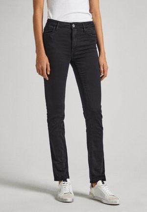 Jeans en denim noir avec une coupe slim, dotés de poches avant, d'une fermeture à un unique bouton et d'une texture lisse. Portés avec des baskets blanches.