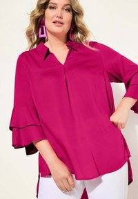 Fuchsia-bluse mit V-Ausschnitt, weit ausgestellten Ärmeln und lockerer Passform. Das Material wirkt leicht und verfügt über einen geraden Saum sowie seitliche Schlitze.