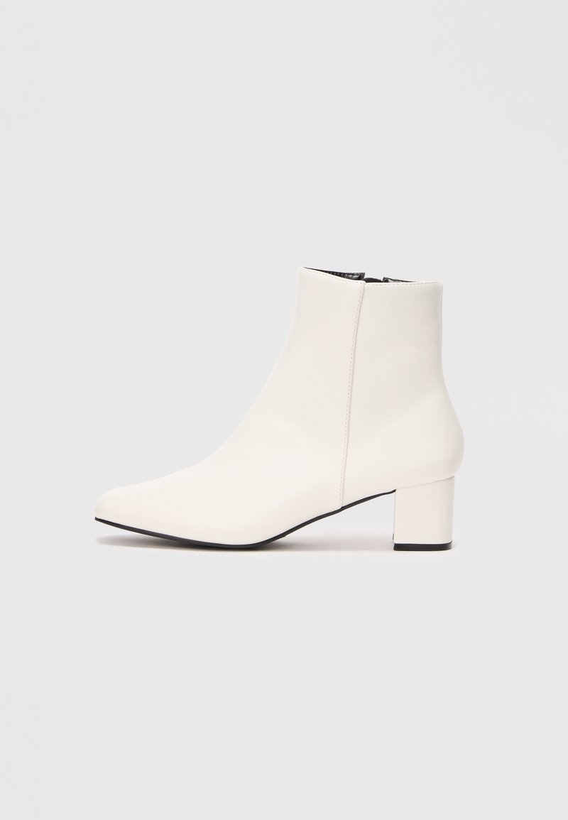 Bottine blanche en cuir avec un bout pointu, un talon bloc et une fermeture éclair sur le côté. Texture lisse avec un design minimaliste.