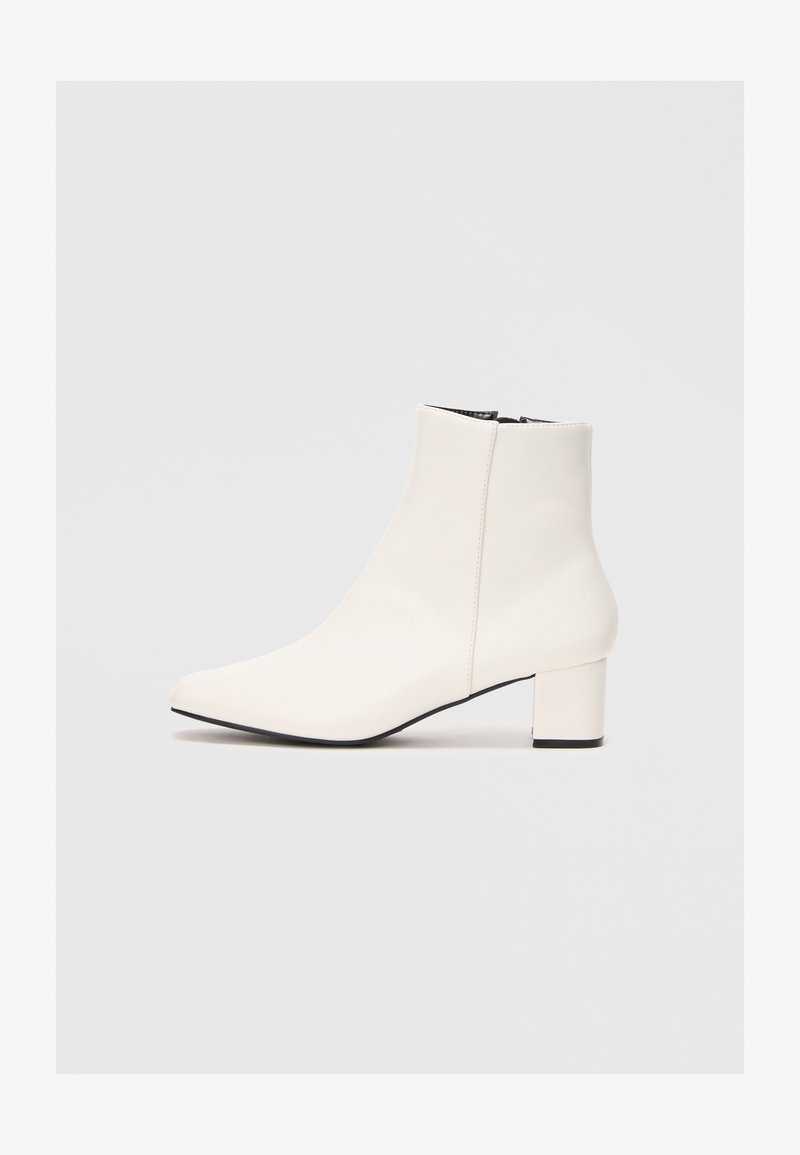 Bottine blanche en cuir avec un bout pointu, un talon bloc et une fermeture éclair sur le côté. Texture lisse avec un design minimaliste.