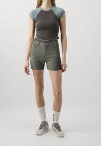 Pantalones cortos de mezclilla verdes ajustados combinados con una camiseta corta negra y verde azulado. Llevados con calcetines blancos y zapatillas grises.