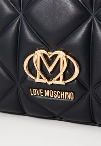 Quilted black faux leather bag featuring a gold "Love Moschino" logo and ornate hardware at the center. Textured geometric detailing throughout.