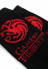 Schwarze Socken mit einem roten Drachenmotiv und dem Schriftzug "GAME OF THRONES", gestrickt in einem kontrastierenden Muster für Sichtbarkeit und Textur.