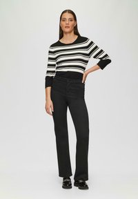 Zwarte rechte broek gecombineerd met een zwart-wit gestreept shirt met lange mouwen. Het shirt heeft een ronde hals en driekwarts mouwen.