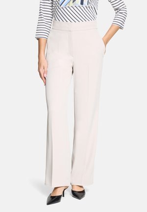 Beige Hosen mit weitem Bein aus glattem Material, ausgestattet mit hohem Bund und Seitentaschen. Kombiniert mit einem gestreiften Langarmoberteil und schwarzen Absätzen.