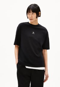 Zwarte katoen t-shirt met een ronde halslijn en korte mouwen. Heeft een klein wit logo op de borst. Soepele textuur en een ontspannen pasvorm.