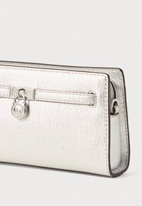 Portafoglio metallico argento con finitura testurizzata, dotato di chiusura con zip, un clasp decorativo e bordi a contrasto.