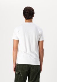 Witte katoenen t-shirt met een ronde hals en korte mouwen, gecombineerd met olijfgroene corduroy broek met frontzakken en een gestructureerde afwerking.