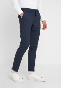 Navy tailored trousers met een textured stof, slim fit en zijzakken, gecombineerd met witte sneakers en een geknoopte witte blouse.
