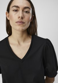 Čierny krátky rukáv top s V-výstrihom a nafúknutými rukávmi. Vyrobený z mäkkej látky, s hladkou textúrou a priliehavým strihom.