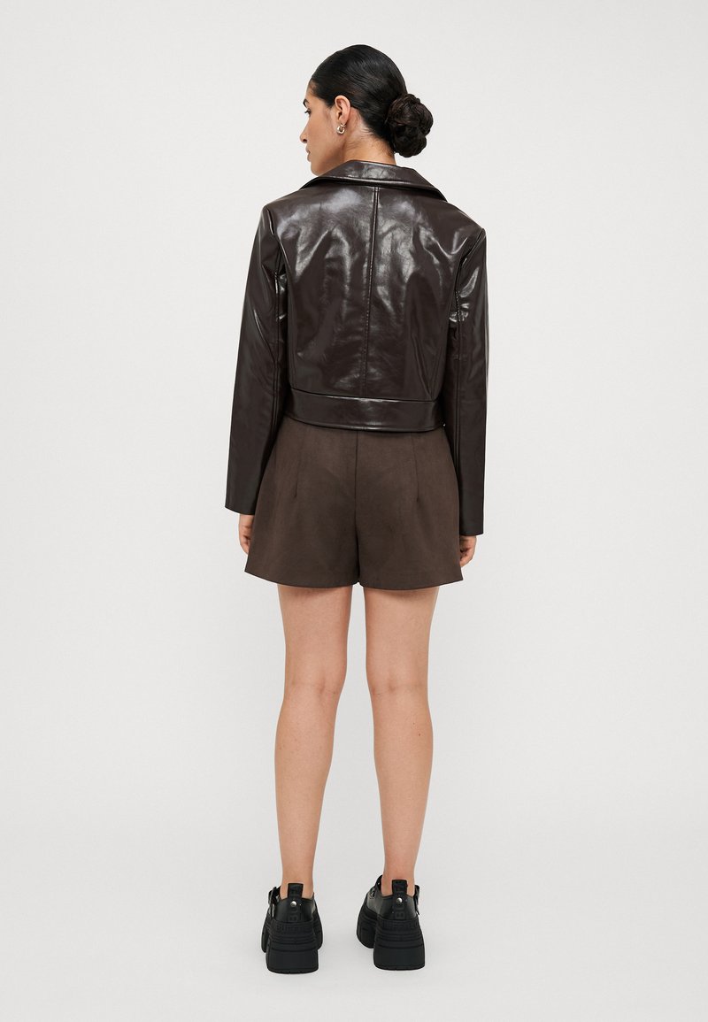 Veste courte en simili cuir marron avec un col pointu et des manches longues, associée à un short marron taille haute et des baskets à plateforme noires.