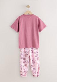 Różowy bawełniany t-shirt z krótkimi rękawami w zestawieniu z różowymi spodniami ozdobionymi kolorowym wzorem kwiatów i uśmiechniętych buziek; ściągacze przy mankietach.