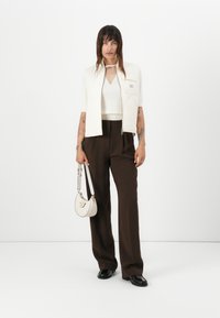 Gilet bianco imbottito con maniche corte, top bianco con scollo a V, pantaloni marroni a vita alta e una piccola borsa bianca con tracolla.