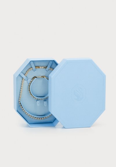 Boîte à bijoux octogonale bleu clair contenant un bracelet et un collier, tous deux ornés d'accents scintillants, posés sur un revêtement en tissu texturé.