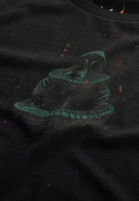 Zwart katoenen T-shirt met een teal grafiek van een stapel banden, met subtiele oranje spikkels en abstracte patronen op de achtergrond.