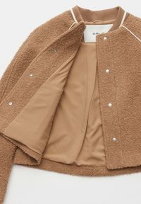 Veste en laine brune texturée avec boutons-pression, doublure intérieure lisse beige, col côtelé avec détail rayé blanc, étalée à plat et ouverte.