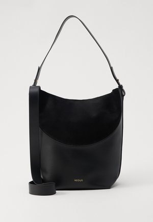 Fekete bőr és velúr válltáska ívelt kialakítással, állítható pánttal és arany logóval az alján. Simma textúra, minimalista stílus.