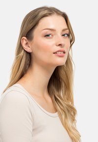 Orecchini a bottone con un semplice design rotondo in argento, caratterizzati da una pietra di colore azzurro chiaro. Il modello ha i capelli lunghi biondi e indossa un top neutro.