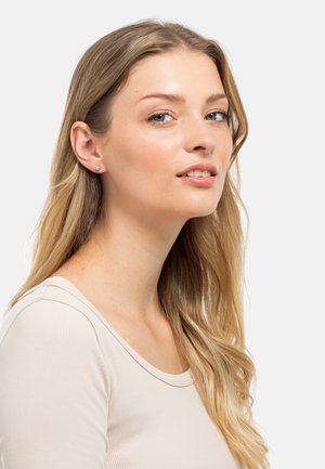 Orecchini a bottone con un semplice design rotondo in argento, caratterizzati da una pietra di colore azzurro chiaro. Il modello ha i capelli lunghi biondi e indossa un top neutro.