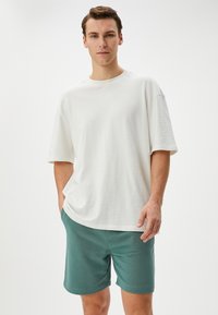 Witte oversized t-shirt met korte mouwen, gecombineerd met teal shorts, gemaakt van zachte stof, met een relaxte pasvorm en subtiele textuur.