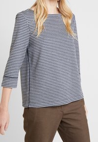 Top med houndstooth-mönster, kvadratisk halsringning och trekvartslånga ärmar. Tillverkad av tyg i marinblått och vitt, med rak fåll.