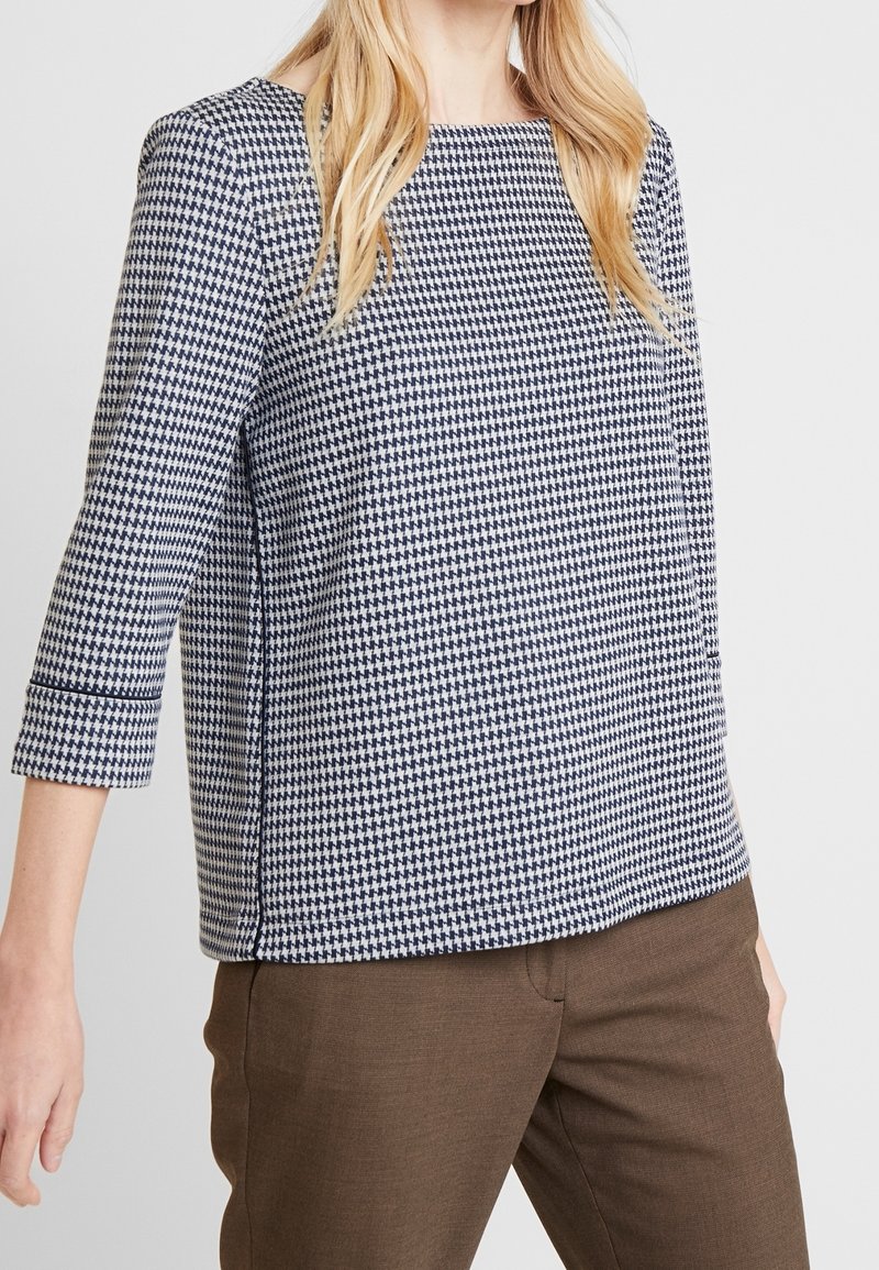 Top med houndstooth-mönster, kvadratisk halsringning och trekvartslånga ärmar. Tillverkad av tyg i marinblått och vitt, med rak fåll.