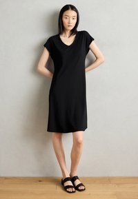 Black short-sleeve dress with a deep V-neck, made of smooth fabric, knee-length cut, paired with simple black slide sandals.