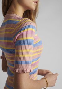 Hedvábný pletený top v pastelově růžových, modrých a žlutých proužcích. Má krátké rukávy s volány, přiléhavý střih a střední délku.
