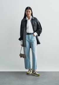 Black leather oversized shirt, white button-up, light blue straight-leg jeans, multicolored sneakers, and a small gray handbag.