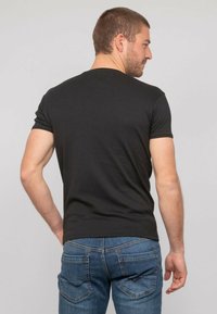 T-shirt noir en coton à manches courtes vu de dos, associé à un jean en denim bleu avec des poches arrière et des détails de couture subtils.