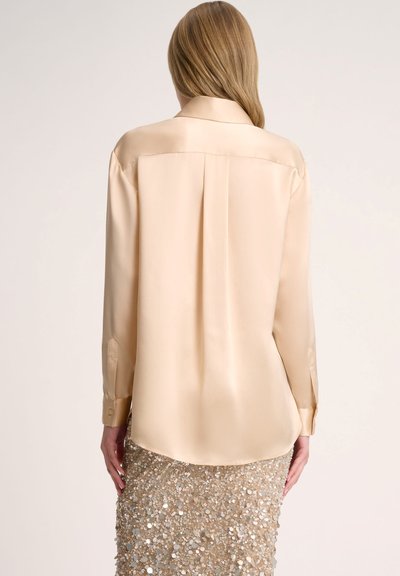 Satin beige blouse with a classic collar, long sleeves, and a back pleat, paired with a sequined gold skirt for added texture and shine.