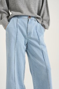 Light blue denim wide-leg pants with side seam detailing, featuring a brown button at the waist. Soft texture, casual fit.