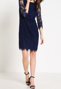 Mörkblå spetsklänning med trekvartsärmar, vågig nederkant, blommönster och en avslappnad passform. Bärs med svarta klackar med remmar.