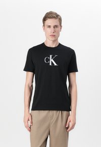 Zwarte katoenen T-shirt met een groot wit "cK"-logo op de borst. Korte mouwen en een klassieke ronde halslijn.