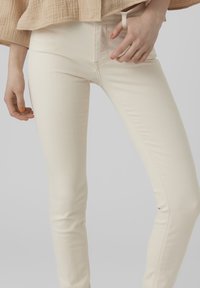 Krémové skinny džíny s hladkým povrchem a minimem švů, vybavené přední kapsou a vysokým pasem.