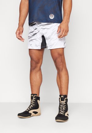 Men's athletic outfit featuring a navy shirt with textured pattern, white and black camo shorts, and black boots with tan accents.