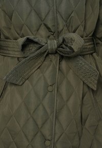 Πράσινο παλτό ελιάς με καπιτονέ σχέδιο, ζώνη στη μέση, διαμάντι μοτίβα, κουμπιά με πατιλέτα και λείο υλικό.