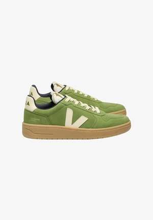 Green suede sneakers with cream accents, featuring a prominent "V" logo and a beige rubber sole. Laces are cream-colored.